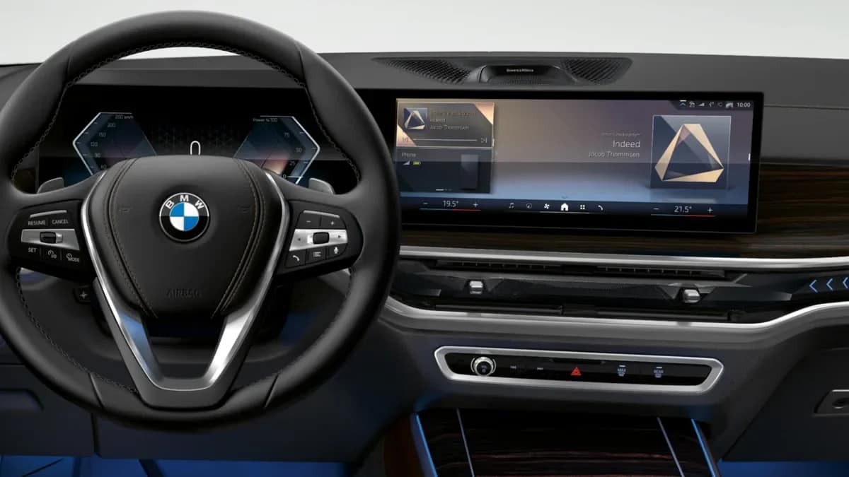Dashboard of the BMW X5 with the curved display, wood trim and a three spoke steering wheel