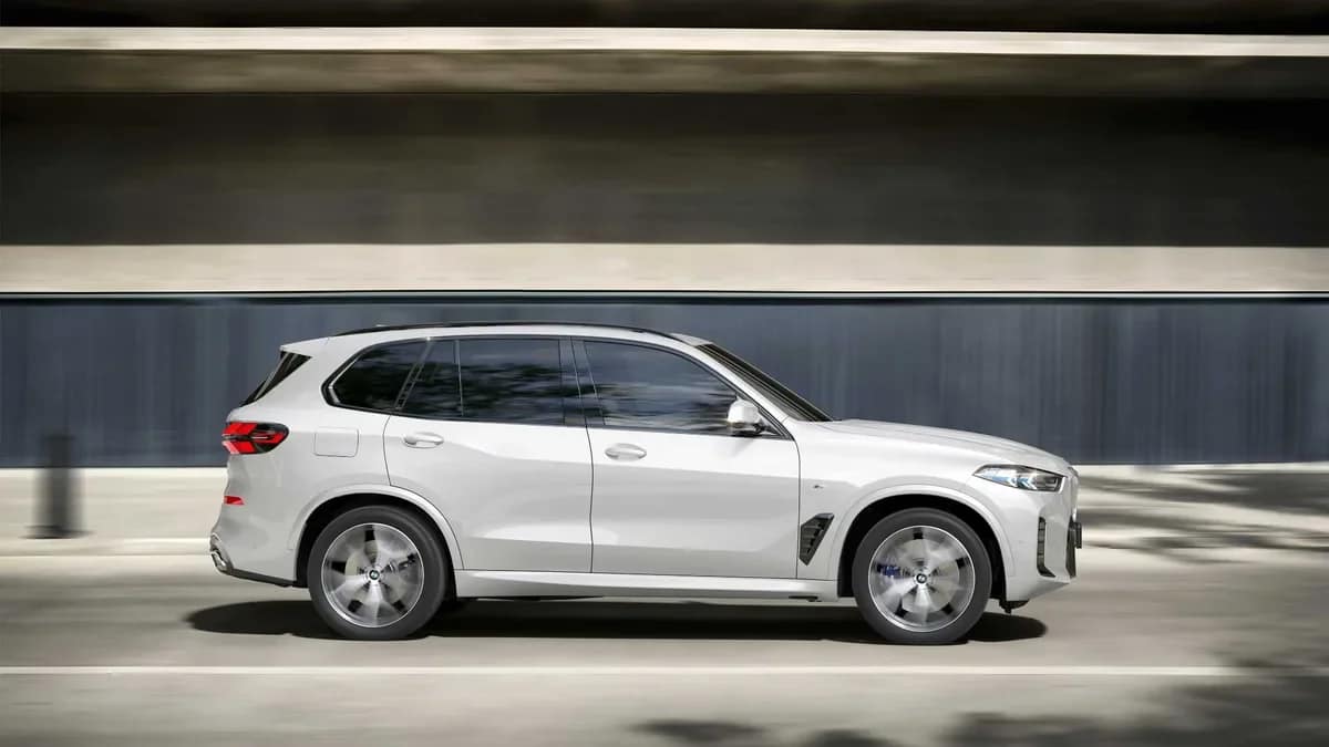 Side profile of a white BMW X5 driving past a building