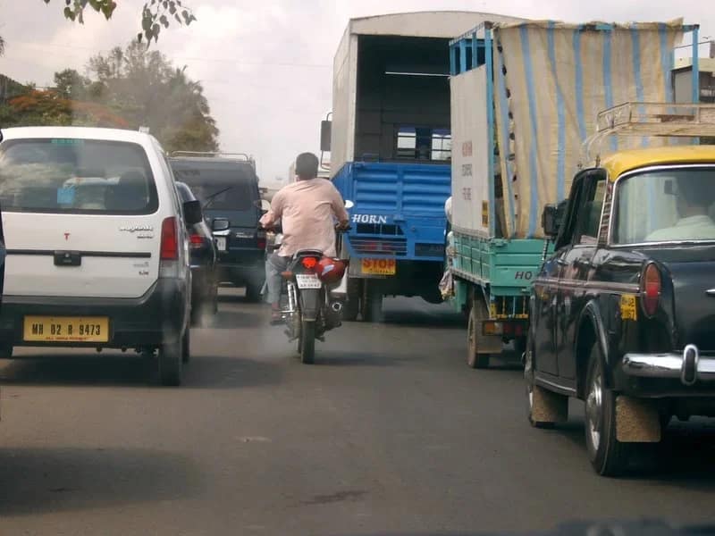 Cars, a motorcycle, trucks and a taxi in slow Bombay traffic with visible exhaust