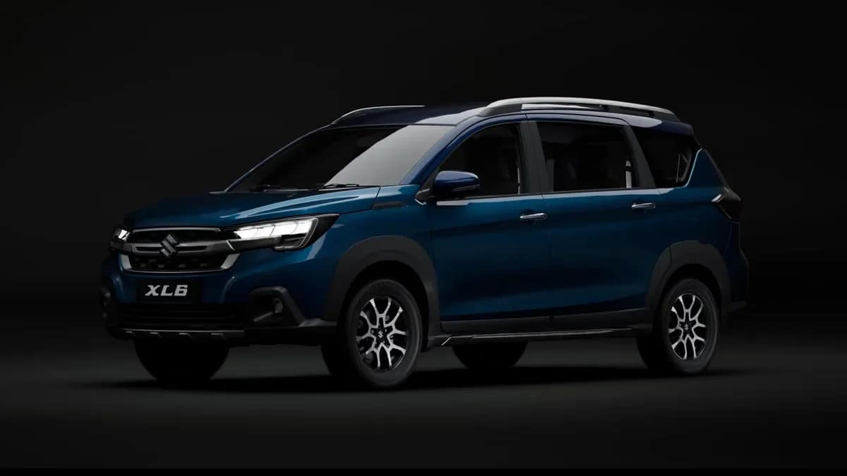 Blue Maruti Suzuki XL6 MPV with silver roof rails on a dark studio background, front three-quarter view