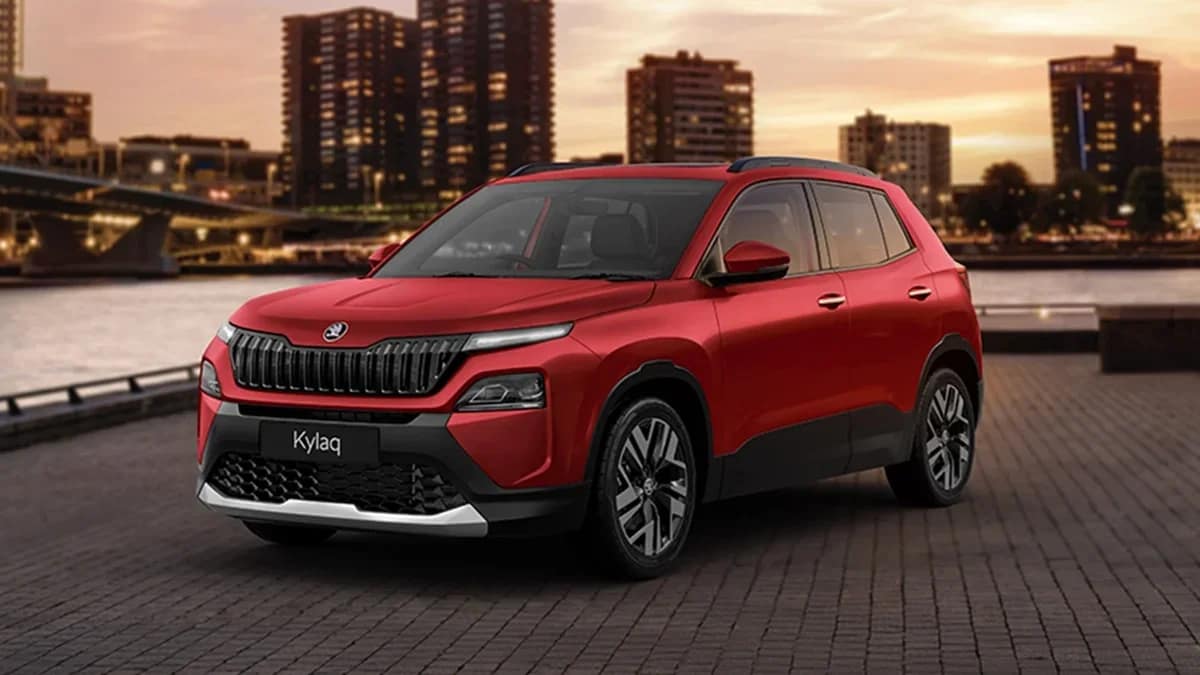 Red Skoda Kylaq compact SUV parked by a river with city buildings in the evening
