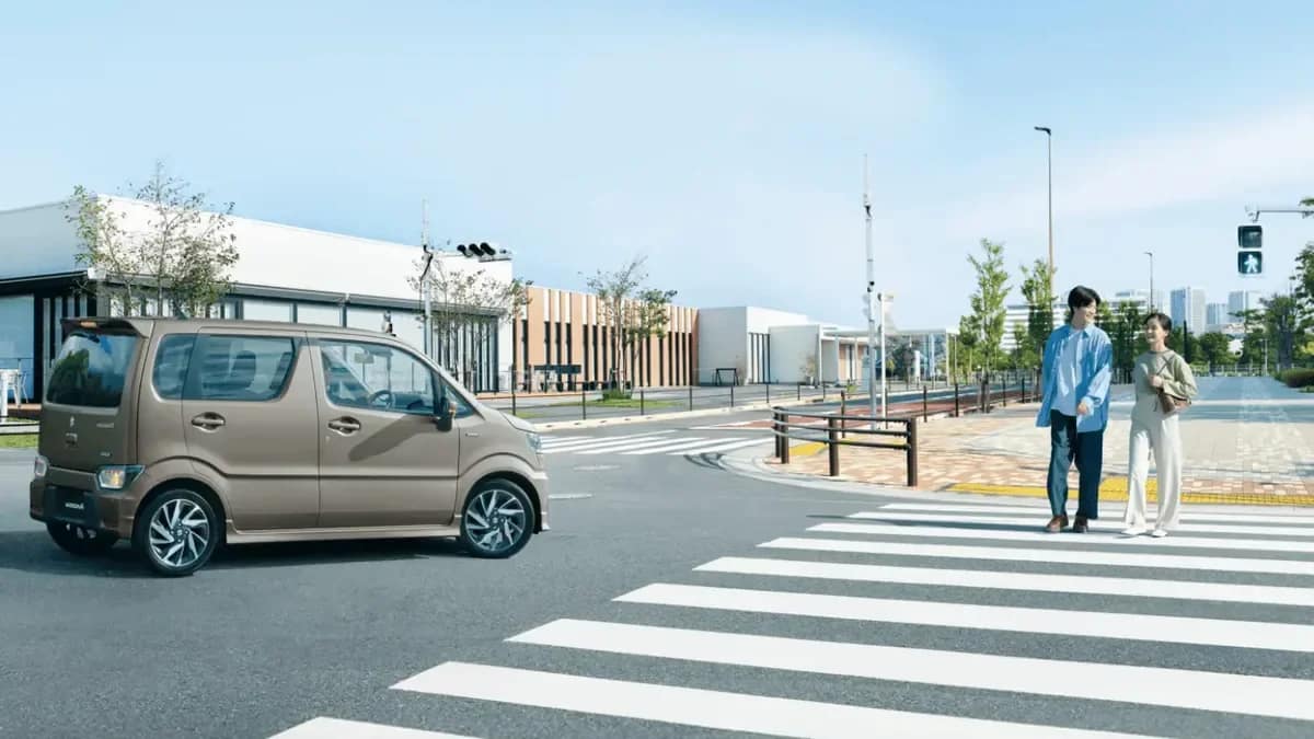 Beige Suzuki WagonR waiting at a road crossing in Japan as people walk past